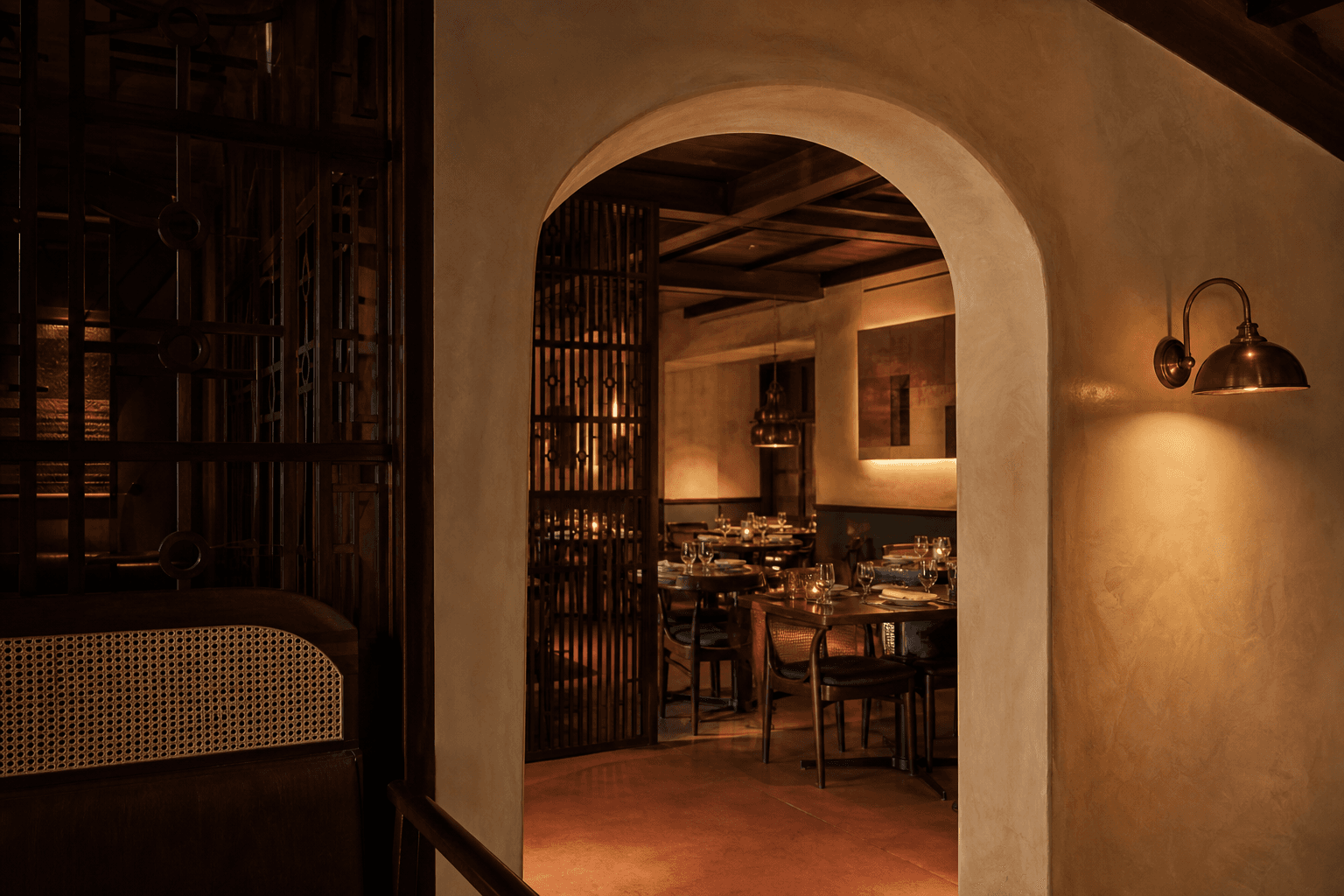 A lime plaster arch and teak screen leading into the restaurant dining room